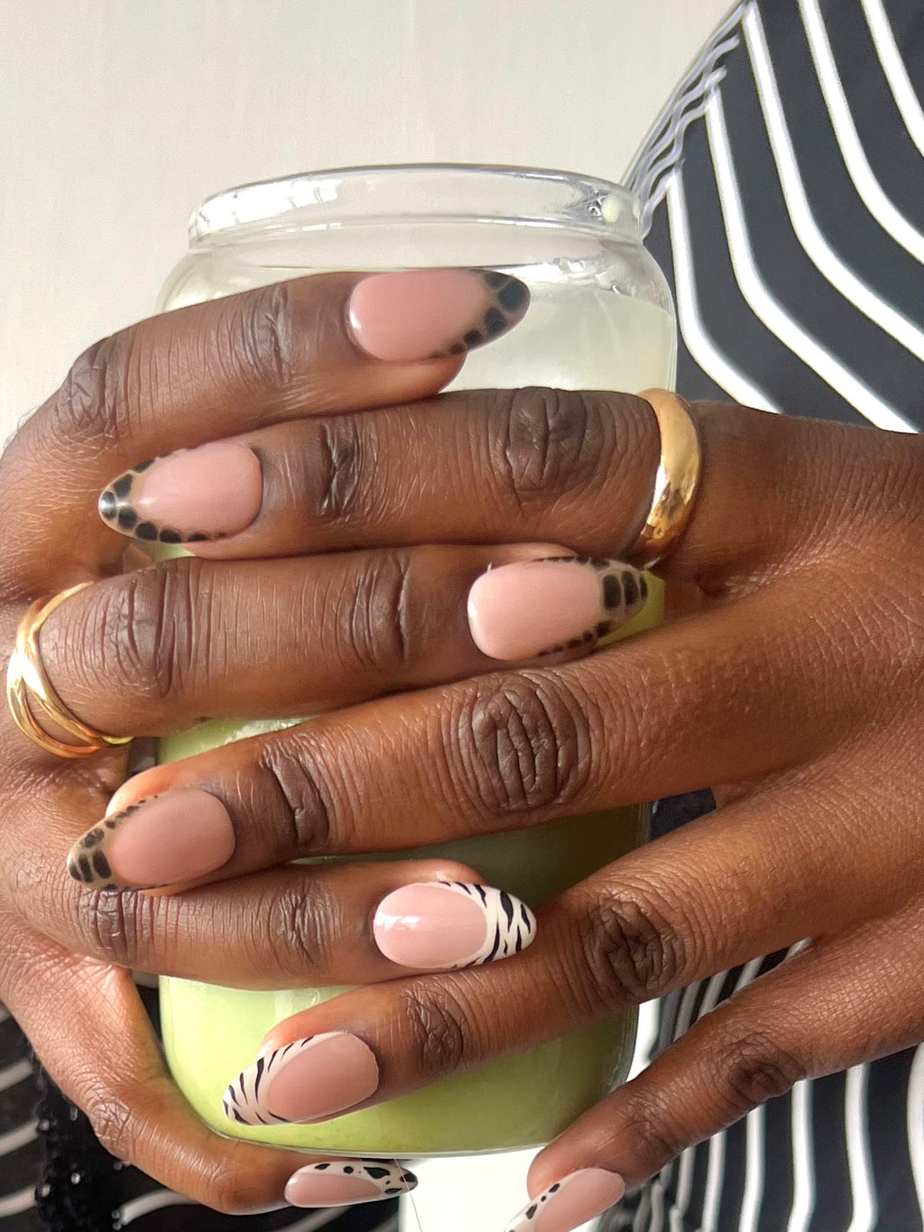 Press-on nails Bold Cherry nude glossy avec motifs animaliers noirs portés avec matcha latte et bijoux dorés